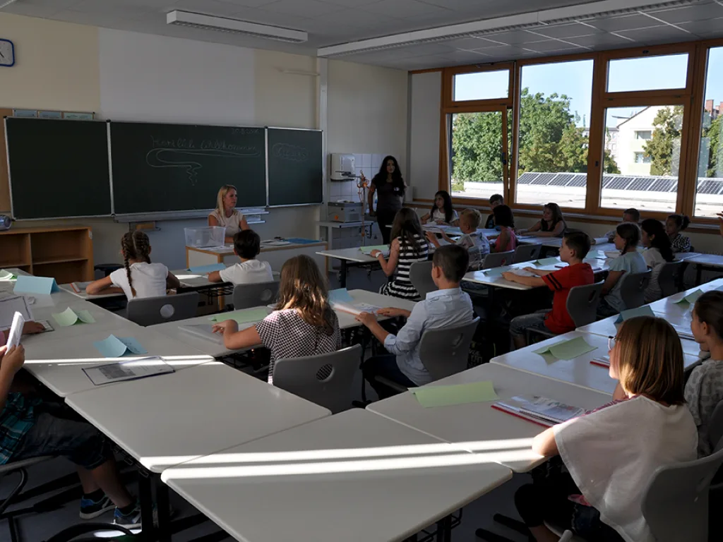 Kinder sitzen an den Tischen und hören zu.